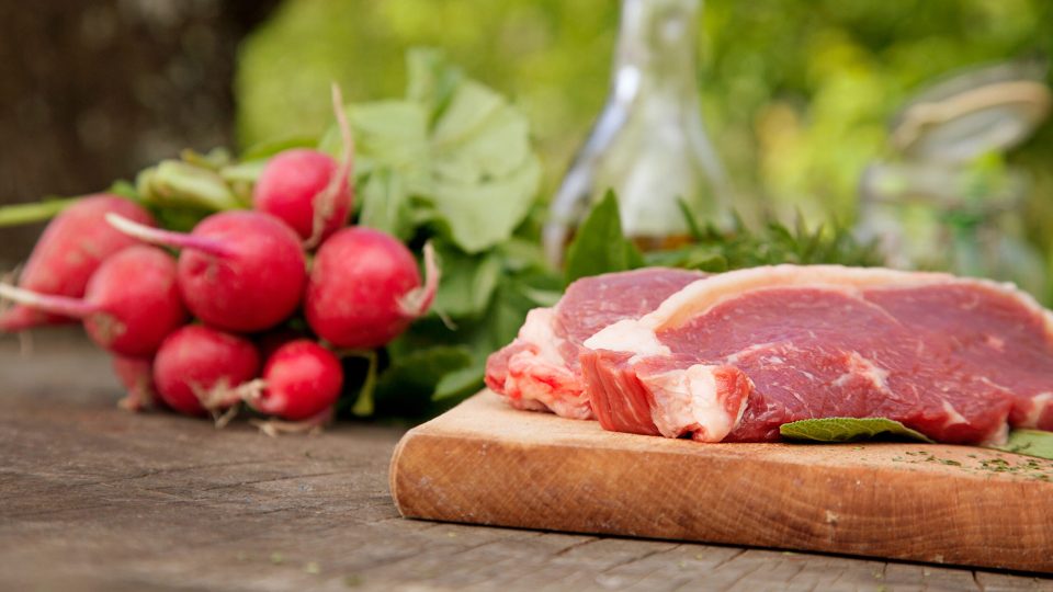 Kött och grönsaker på trä-skärbräda med grönskande bakgrund.